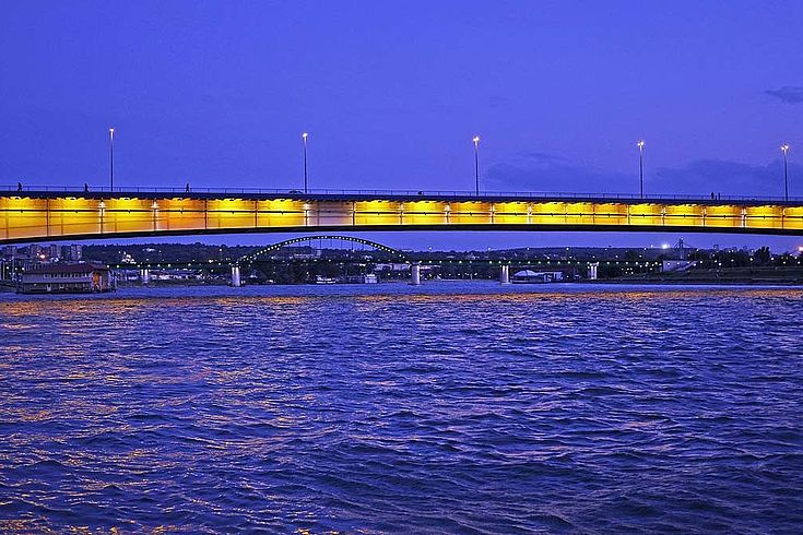 Langgezogene Brücke in Belgrad über dunklem Wasser bei Nacht.